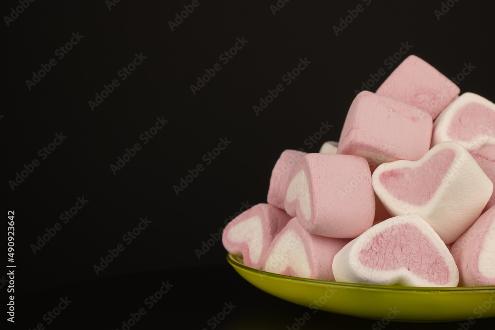Colored marshmallows sweets in the saucer on black background. Dessert pink and white in the form of hearts. Cooking concept delicious sweet food. Colored marshmallows sweets in the saucer on black background. Dessert pink and white in the form of hearts. Cooking concept delicious sweet food.