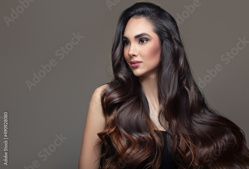Brunette woman with black wavy ombre hair. Portrait on a gray background