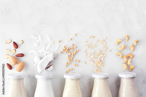 Vegan, plant based, non dairy milk. Variety in milk bottles with ingredients. Above view over a white marble background.