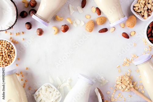 Vegan  plant based  nondairy milk frame. Variety of types in milk bottles with scattered ingredients. Overhead view on a white marble background with copy space.