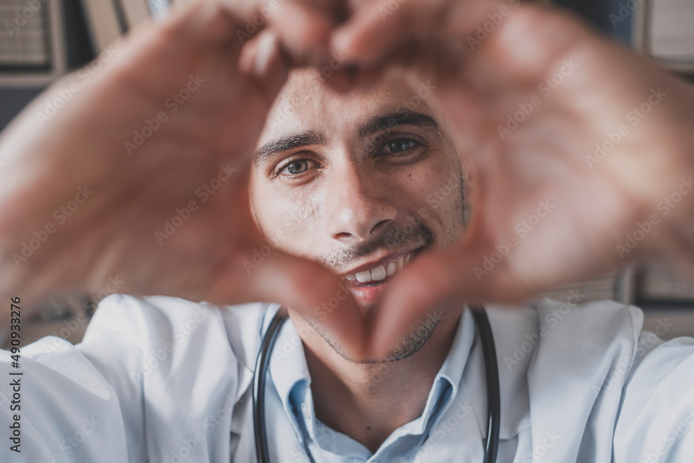 Happy young male doctor showing support and care to patients or client in hospital. Portrait of handsome man healthcare worker making love heart sign with hands at medical clinic