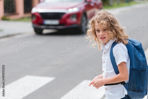 Cute little boy with a blue backpack crosses the street