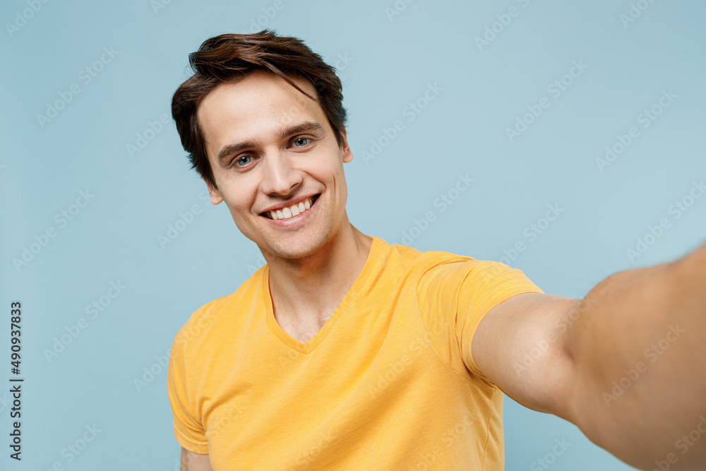 Close up young smiling happy cheerful fun man 20s wear yellow t-shirt doing selfie shot pov on mobile phone isolated on plain pastel light blue background studio portrait. People lifestyle concept Close up young smiling happy cheerful fun man 20s wear yellow t-shirt doing selfie shot pov on mobile phone isolated on plain pastel light blue background studio portrait. People lifestyle concept