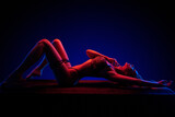 Beautiful young brunnete girl lying in sexy lingerie in colored light in studio on a dark background