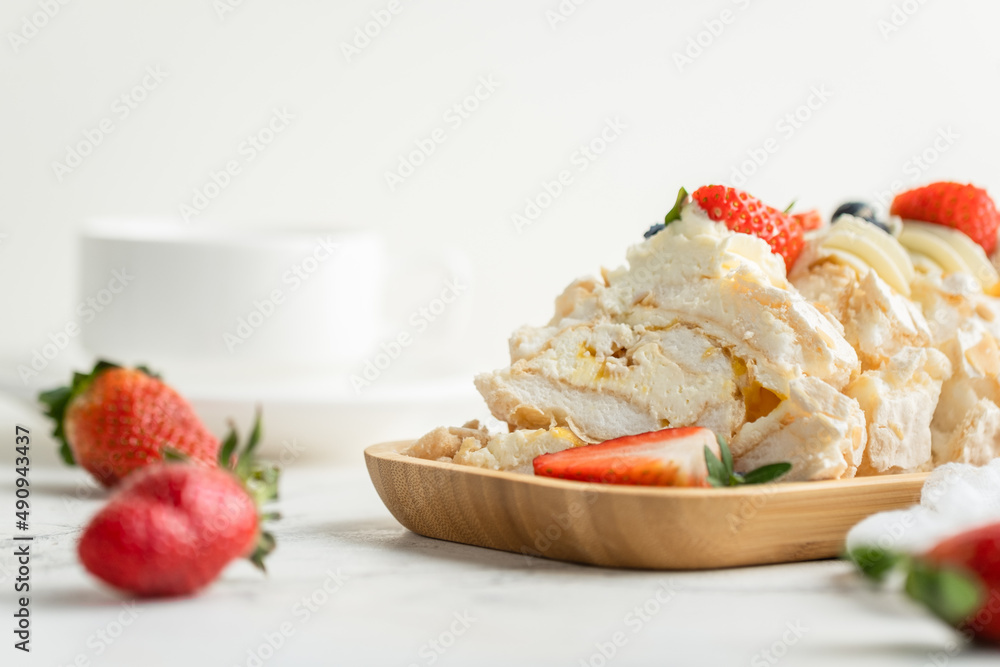 Meringue roll decorated with strawberries and blueberries sliced and served in the wooden plate on the white background. Macro shot Meringue roll decorated with strawberries and blueberries sliced and served in the wooden plate on the white background. Macro shot