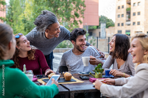 group of multiethnic friends having breakfast with coffee  cappuccino and chocolate muffin  meeting of young people outdoors at a coffee shop