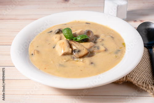 Homemade cream of chicken and mushroom soup or French style chicken fricassee, in a white soup bowl on a wooden table. High view.