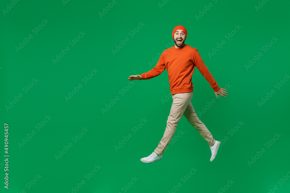 Full body young happy overjoyed excited fun cool man 20s wearing orange sweatshirt hat jump high walking going hurrying celebrate isolated on plain green background studio People lifestyle concept Full body young happy overjoyed excited fun cool man 20s wearing orange sweatshirt hat jump high walking going hurrying celebrate isolated on plain green background studio People lifestyle concept