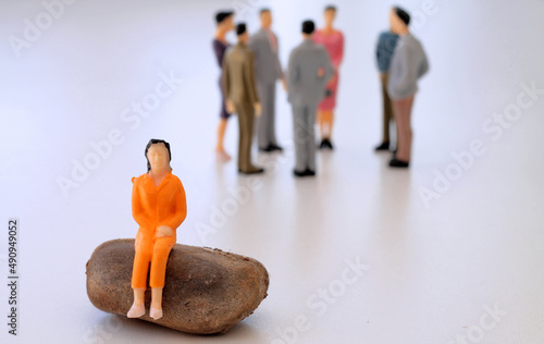 Woman sitting alone excluded from the group of people communicating behind her - symbolised by small figurines photo