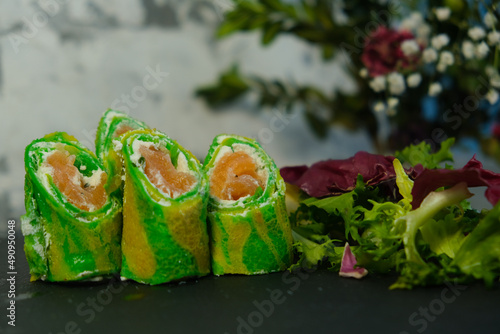 Green pancakes, folded dough rolls, serving pancakes for Shrovetide. Filled with salmon and tender cheese. Zebra dough. Unusual serving food. Cooking, delicious food, colorful food.