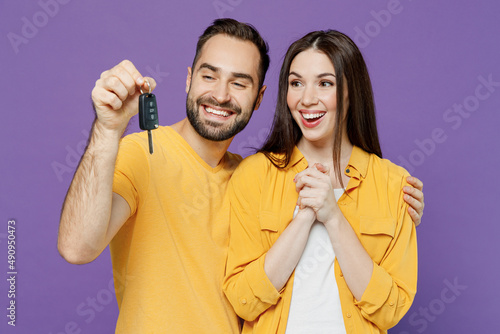 Young smiling satisfied happy fun couple two friends family man woman together wear yellow clothes looking camera hold car key fob keyless system isolated on plain violet background studio portrait.