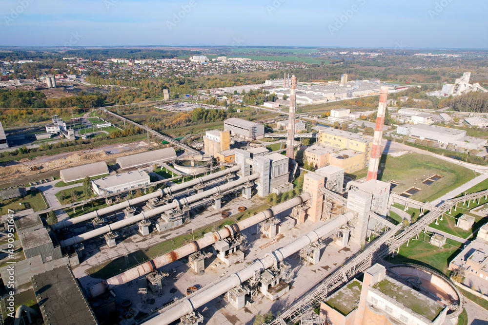 Fototapeta premium Industrial plant, aerial view. Cement plant with pipes on cement production. Factory with smoke pipe. Chimney smokestack emission. Poor environment. Ecology concept, air and environmental pollution.