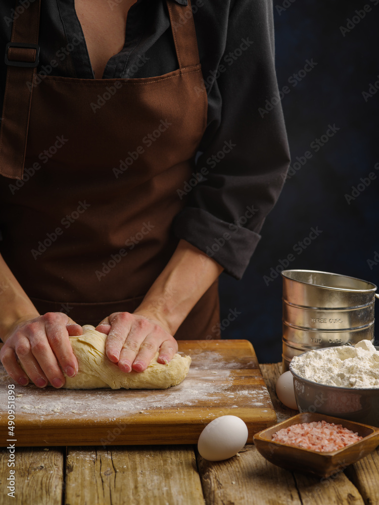 Macro shot. Preparation of dough by the hands of a professional chef on a wooden cutting board, dark background. The concept is the preparation of bread, pizza, pasta, pie, confectionery. Macro shot. Preparation of dough by the hands of a professional chef on a wooden cutting board, dark background. The concept is the preparation of bread, pizza, pasta, pie, confectionery.