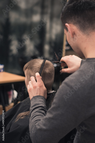 Toddler boy happy to be on the haircut with a professional children's hairdresser. little boy having a haircut at hair salon. Hairdresser's hands making hairstyle to child