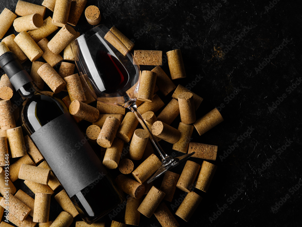 On a black background a lot of wine corks, a bottle of red wine and a wine glass. Romantic date, holiday, banquet, restaurant, hotel, bar, advertising, banner, poster.