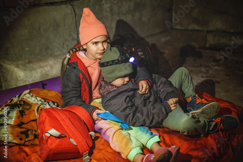 Thoughtful little kids with Ukrainian flag lay in a bomb shelter and waits for the end of the air attack of Russian invaders, terrorism and war, current history photo