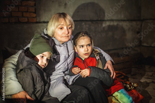 Grandmother hugs her little kids while they sit out the attack of the Russian aggressor in a bomb shelter. Terrorism and war, current Ukrainian and world history photo