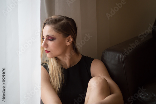 Millennial woman in black dress and makeup sitting at the window © hellame