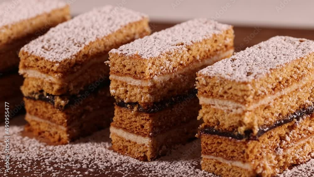 Traditional homemade Romanian Honey Layered Cake with plum jam and semolina cream also called Albinita or Dulcineea. Sprinkling sugar powder on top of cut portions of cake. Traditional homemade Romanian Honey Layered Cake with plum jam and semolina cream also called Albinita or Dulcineea. Sprinkling sugar powder on top of cut portions of cake.
