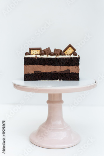 Chocolate cake with cream sponge cake decorated with cookies stands on a white stand on a white background. Isolated background. A tasty treat for a children's birthday party. Pastry craftsmanship.