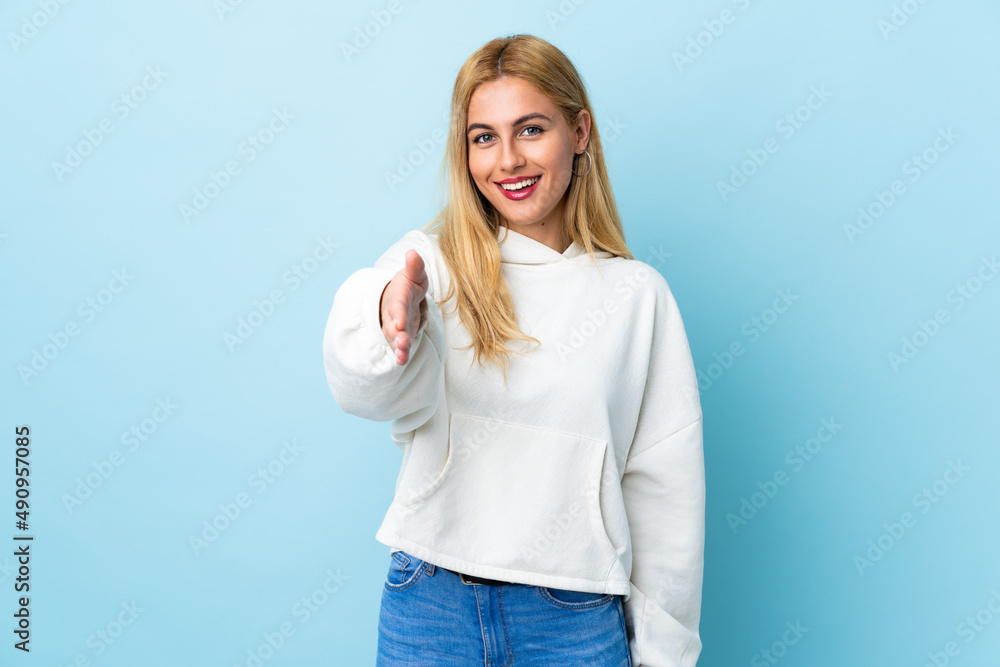 Fototapeta premium Young Uruguayan blonde woman over isolated blue background shaking hands for closing a good deal