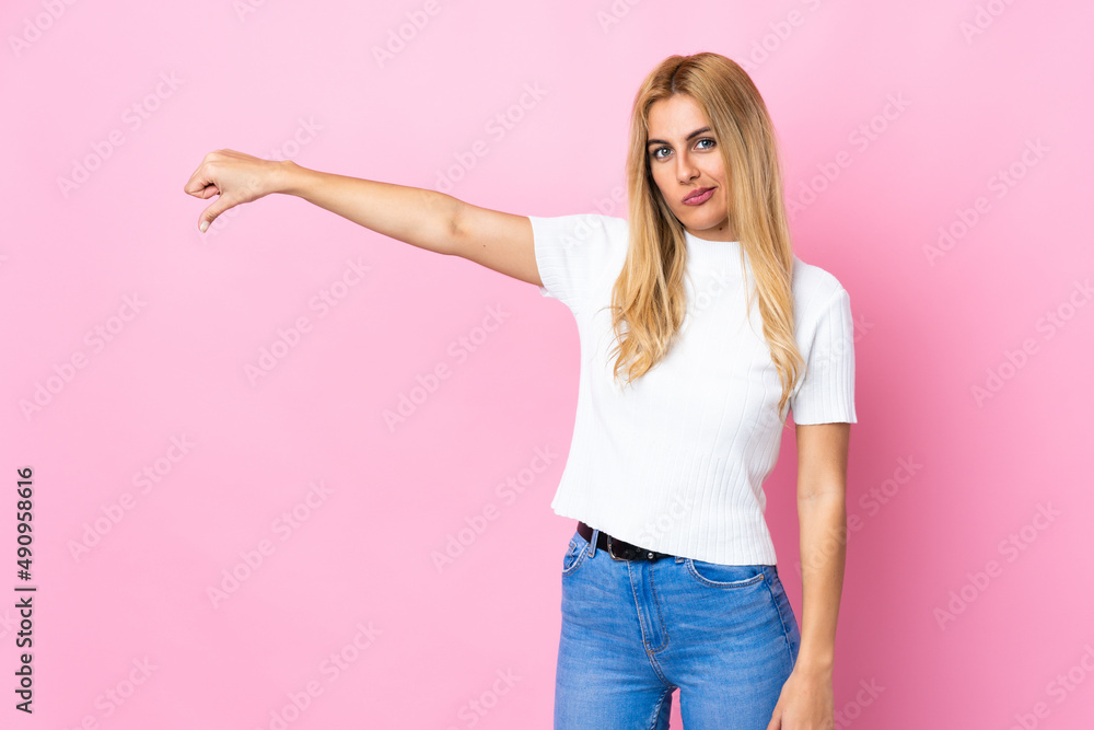 Young Uruguayan blonde woman over isolated pink background showing thumb down with negative expression Young Uruguayan blonde woman over isolated pink background showing thumb down with negative expression