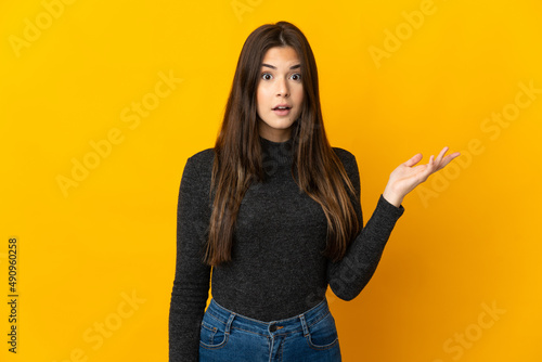 Teenager Brazilian girl isolated on yellow background making doubts gesture