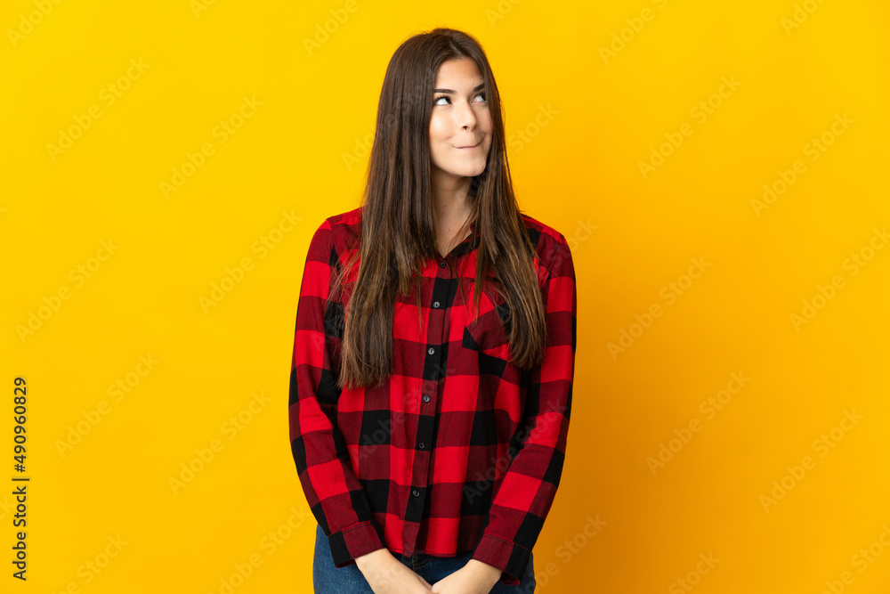 Teenager Brazilian girl isolated on yellow background having doubts while looking up