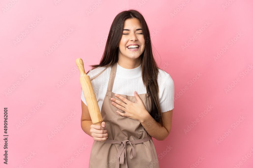 Teenager Brazilian girl holding a rolling pin isolated on pink background smiling a lot Teenager Brazilian girl holding a rolling pin isolated on pink background smiling a lot