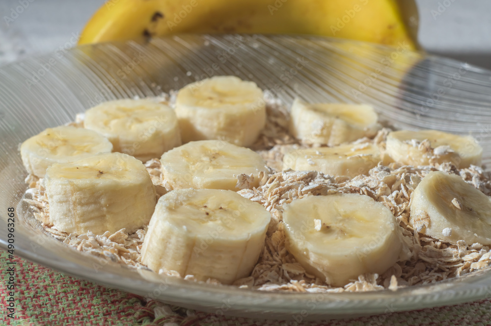 flaked oats and sliced banana, on a plate that is on a table with natural light,copy space in several parts
