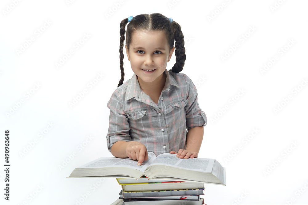 charming little girl with braided pigtails sits in front of a large book and looks into the camera charming little girl with braided pigtails sits in front of a large book and looks into the camera