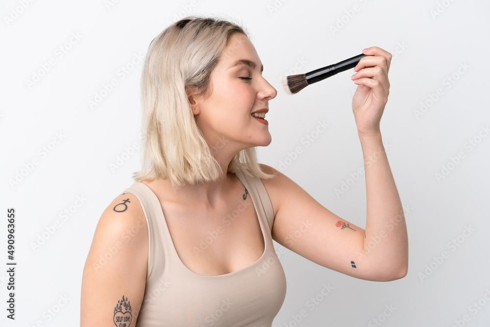 Fototapeta premium Young caucasian woman isolated on white background holding makeup brush and whit happy expression