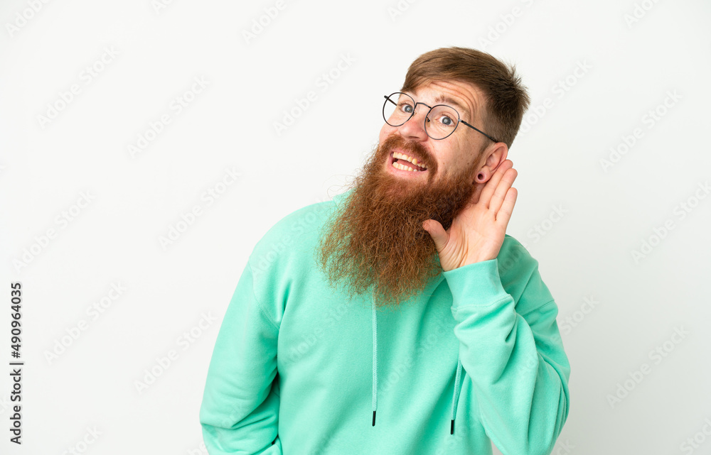Young reddish caucasian man isolated on white background listening to something by putting hand on the ear