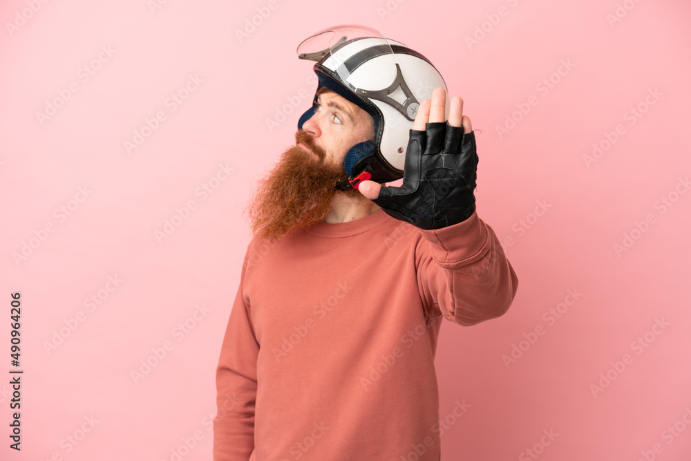 Obraz premium Young reddish caucasian man with a motorcycle helmet isolated on pink background making stop gesture and disappointed