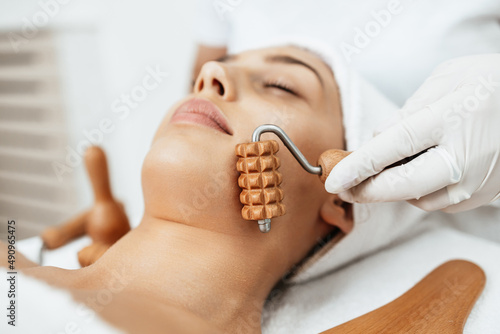 Beautiful brunette getting face maderotherapy in a beauty salon. Professional skin care treatment. photo