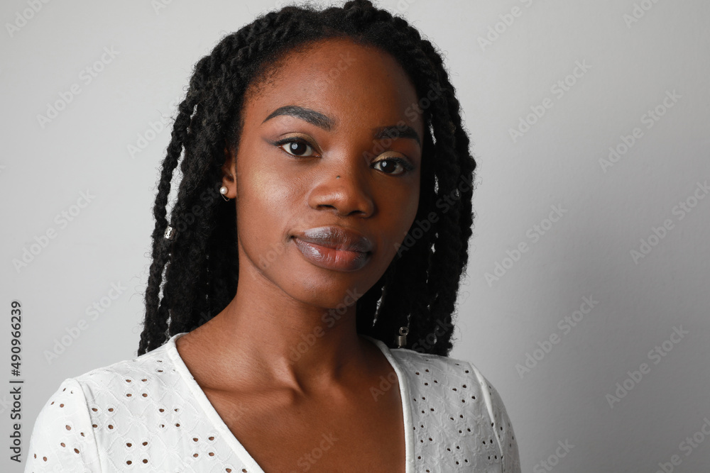 Positive and happy young African woman with long braids posing over white wall. - obrazy, fototapety, plakaty 