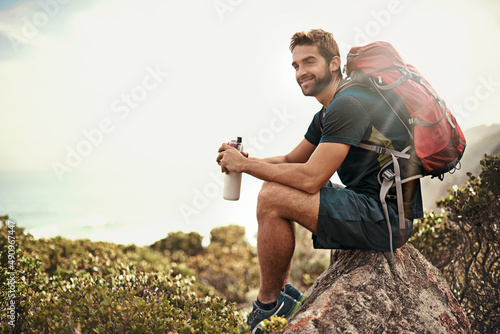 The perfect day to be out in nature.... Shot of a young man taking a water break while out hiking. photo