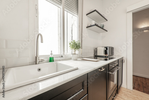 Kitchen with dark wood furniture with white marble top, porcelain sink, ceramic hob, aluminum window, ficus benjamina and countertop microwave oven