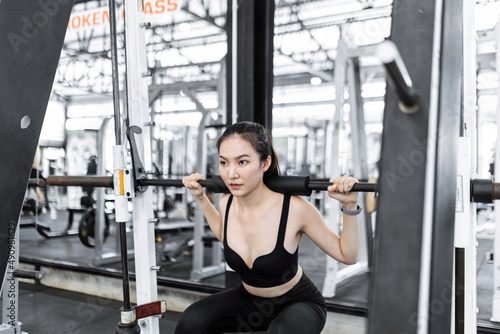 exercise concept The woman in black sport outfits carrying doing weight machine by carrying it on her shoulders and trying to lift it up