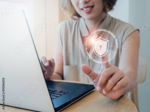 Cyber security, personal data protection, and business privacy concept. Shield and lock icon in the air while woman scanned by her finger for access identification while using laptop computer. photo