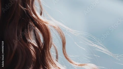 Woman with curly red hair locks waved by light wind at bright sunlight closeup slow motion. Pretty lady with elegant hairstyle. Beauty and fashion