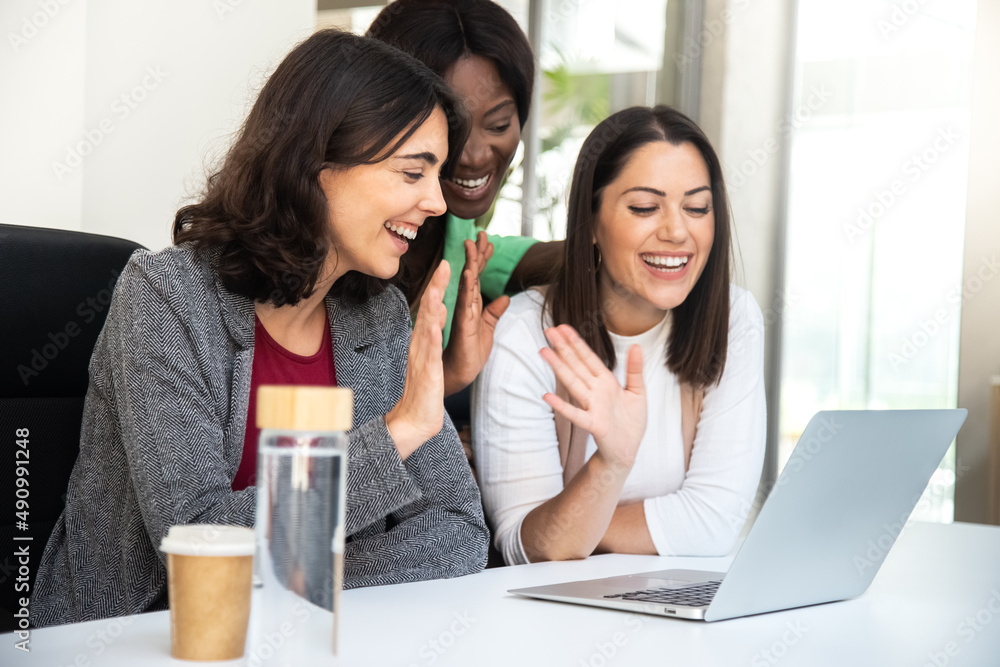 Smiling multiracial coworker women wave hello during business video call using laptop. Smiling multiracial coworker women wave hello during business video call using laptop.