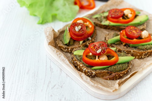 Vegan sandwiches with rye bread and vegetables on a wooden tray on a white table. A healthy breakfast or snack. Side view. Space for text. Close-up. Dietary nutrition.