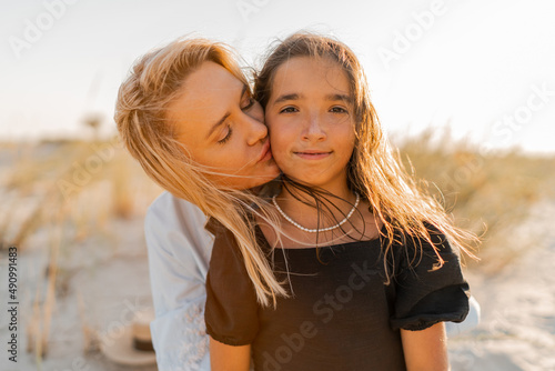 Beautiful blond mother  and  brunette daughter  posing  on the beach in  warm sunset light. Happy family resting at beach in summer.
