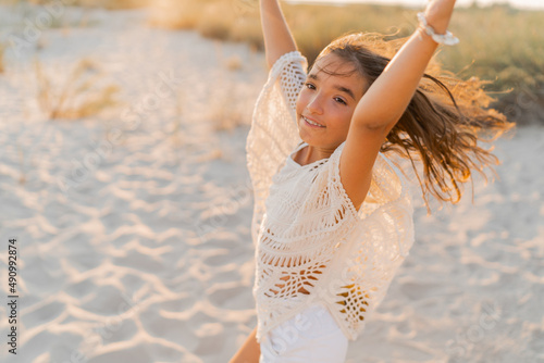 Small girl in stylish boho outfit  having fun and jumping  on the beach. Warm sunset colors. Wacation and  travel concept. photo