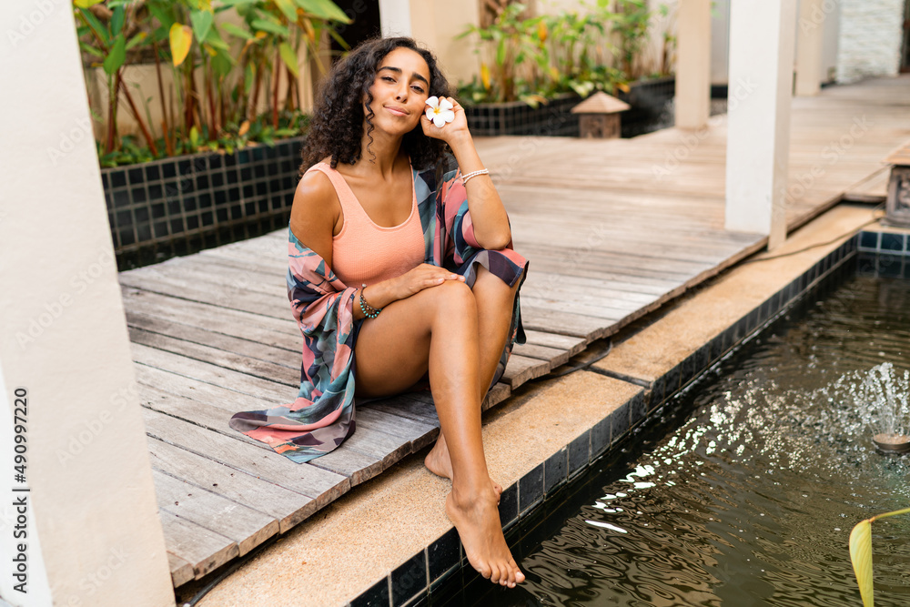 Blissful woman with tropical flower posing in luxury spa hotel while traveling.
