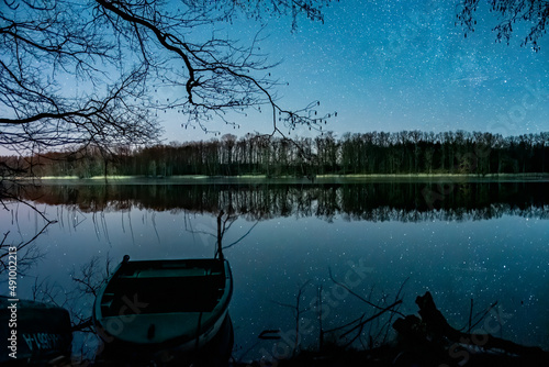 Łódka nad jeziorem w trakcie pogodnej nocy. Łódź lub statek i gwiazdy. Łowienie ryb nocą.