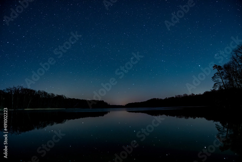 Nocne niebo nad jeziorem. Widok odbijających się gwiazd w lustrze wody.