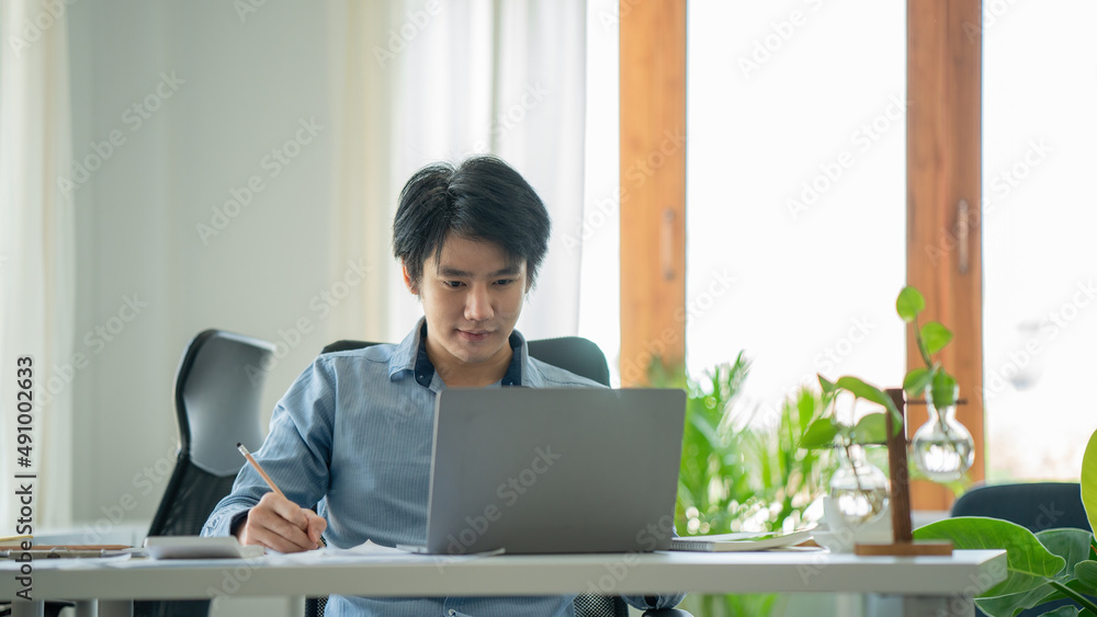 Young asian businessman smiling while working with laptop computer at office, business office lifestyle concept Young asian businessman smiling while working with laptop computer at office, business office lifestyle concept