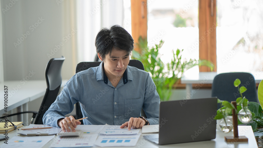 Asian businessman works in the office, calculates the report, the financier on paper works, uses the laptop and the calculator Asian businessman works in the office, calculates the report, the financier on paper works, uses the laptop and the calculator